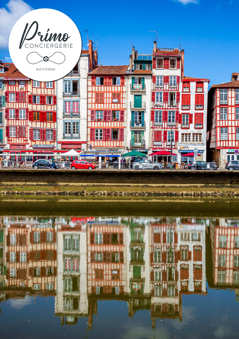 Photographie colorée des maisons traditionnelles de Bayonne, avec leurs façades rouges et blanches, reflétées sur l'eau.
