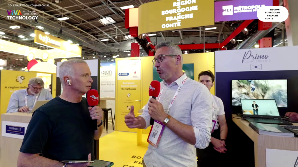 Image tirée du live Twitch de Samuel Etienne. Le stand de Primo Conciergerie lors de VivaTech 2025 est en arrière-plan pendant que Samuel Etienne fait une interview sur le stand de la région Bourgogne-Franche-Comté.